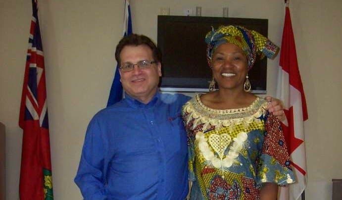 man wearing blue shirt next to woman wearing gold, red, blue outfit, black tv hanging in the background